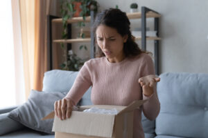 Displeased woman looks at broken item in packaging.