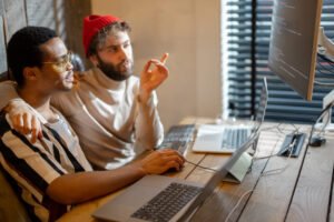 Two men sit at cozy home office discussing investing options.