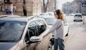 Woman reaches to open her car door, which is parked on a city street.