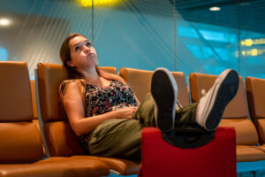 Woman at the airport sits with her feet on her carry on bag, bored of waiting for her checked bag.