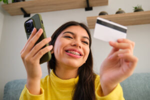 Teenage girl with braces looking at credit card in one hand and cellphone in the other.