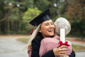 College graduate holds diploma while smiling and hugging parent.