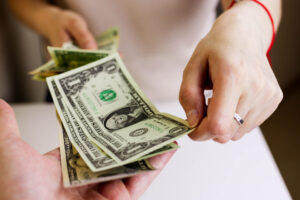 Hands pass dollar bills to another in a business setting.