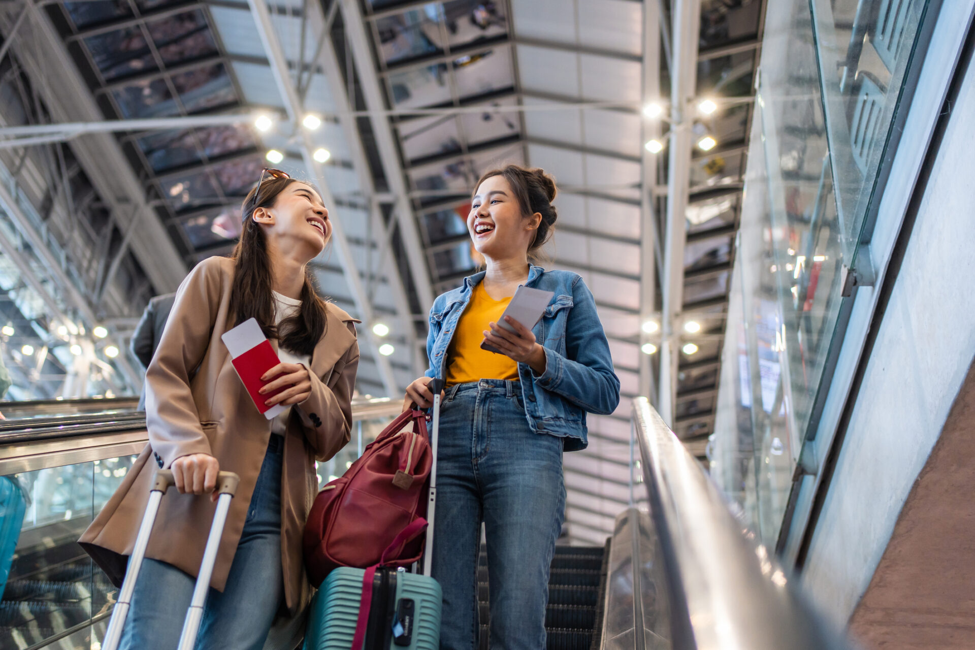 Two female friends wait in the airport together before boarding their flight.