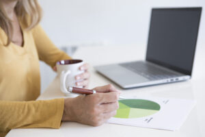 Hands of a woman drinking a cup of tea while analyzing a pie graph.