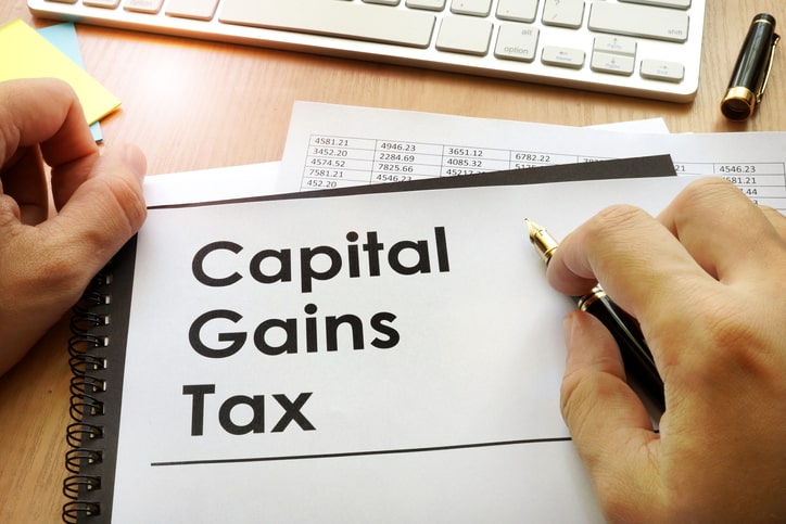 Hand holding a pen and a capital gains tax document: Guide on the difference between short-term vs. long-term capital gains