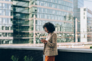 Woman in a downtown setting, surrounded by buildings and looking at her phone.