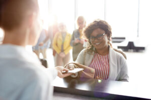 Happy young traveler giving registration manager her passport for check-in while standing by counter.