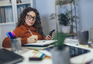 Woman holding phone in her hands, calculating budget at home.