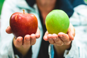 Close-up shot of a woman holding out a red apple and green apple, each in one hand.