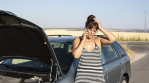 Upset woman driver with broken car using mobile phone during car trouble.