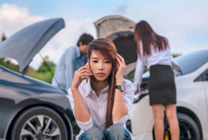 Woman on cellphone in between two cars with hoods up and drivers examining the damage.