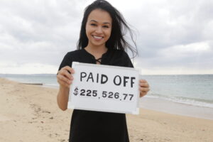 Erika Kullberg standing on a beach and holding up a sign that says Paid Off $225,526.77