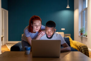 Woman leans over partner's shoulder to read laptop screen showing financial guide.