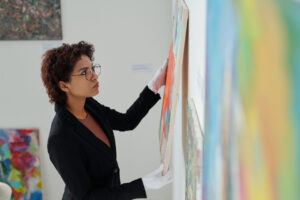 Young woman in white gloves hanging paintings on a gallery wall.