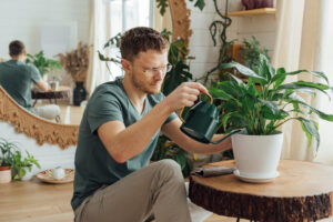 Man waters plants at home from a watering can.