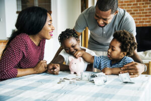 Parents with two children at a table putting money into a piggy bank