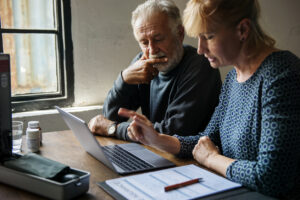 Elderly couple looking at a laptop and paperwork and reviewing life insurance plan.