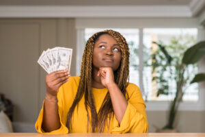 African American woman holding dollars and thinking.