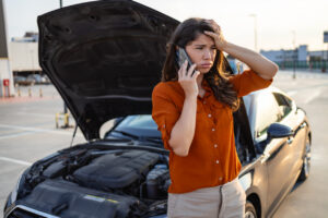 Woman with car hood open calls car insurance.