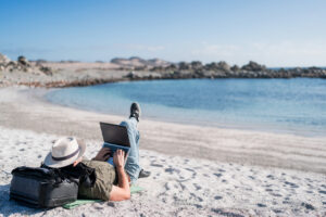 Digital nomad lying on the beach and working on a laptop.