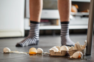 Broken eggs on a kitchen floor, with a person's feet in the background.