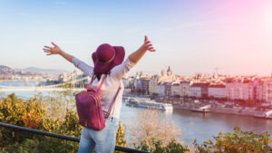 A happy young woman in purple hat enjoying her trip to Budapest, Hungary, from a hilltop during sunrise in autumn.