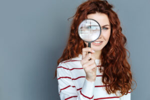 A cheerful woman holding a magnifying glass to her eye.