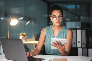 Business woman reading finance portfolio on a tablet, at a desk with a laptop.