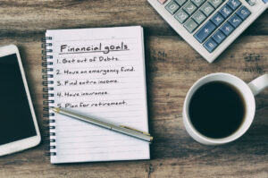 A notepad that lists out financial goals, with a calculator and coffee beside it.