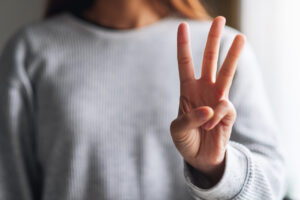 Close-up image of a woman making a number three hand sign.
