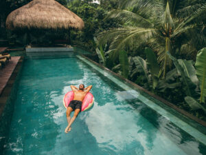 Man floating in a donut-shaped inflatable ring in a pool in the tropics.