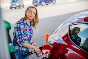 Blonde woman filling her red car with gasoline at a gas station.