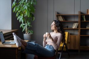 Young woman relaxing at home with bare feet on desk, drinking tea or coffee.