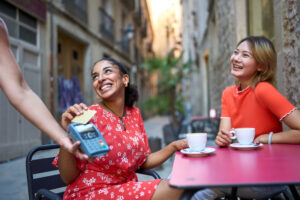 Two women pay with a credit card at an outdoor cafe while traveling.