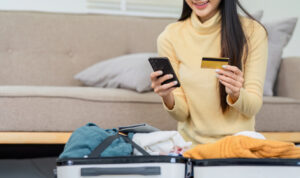 Young woman uses credit card for booking flight while packing her suitcase.
