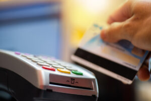 A close-up of a person's hand, running a credit card through a processing machine.