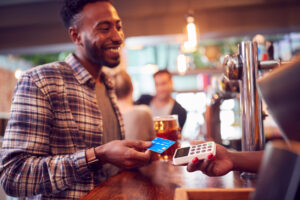 Smiling Black male customer paying with credit card at a bar.