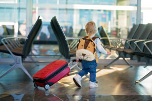 Toddler wearing a lion backpack and pulling a suitcase through the airport.