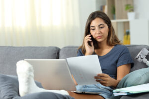Woman with injured foot holding paperwork calls insurance agency.
