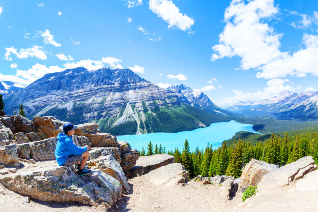 Boy sitting on a rock, looking out over a lake, forests and mountains