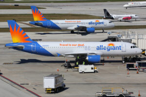 Two Allegiant airplanes parked at their gates with ground crew coming out