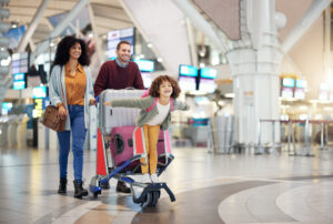 Parents and child walk through the airport with a suitcase trolley.