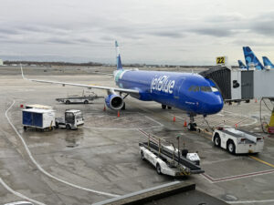 A JetBlue airplane parked at the gate with baggage carts on the tarmac