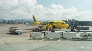 A Spirit airplane on the tarmac with luggage carts