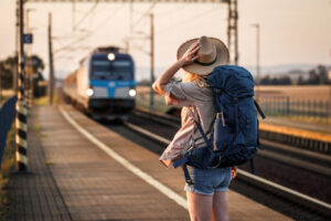Woman traveler with backpack, waiting on train platform and watching the incoming train
