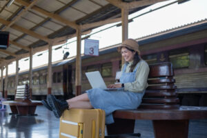 Young female traveler uses her laptop while waiting in a train station with her luggage.