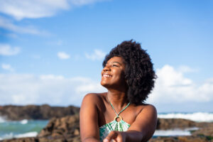 Portrait of a smiling woman wearing sundress, sitting on the rock of a beach looking to the side
