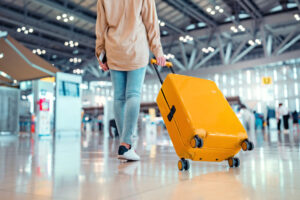 Back view of a traveler pulling their yellow suitcase through an airport