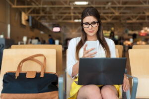 Professional woman sitting in airport waiting area with her laptop and baggage.